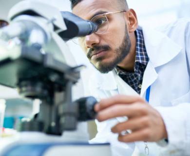 Middle Eastern Man in white lab coat looks into microscope