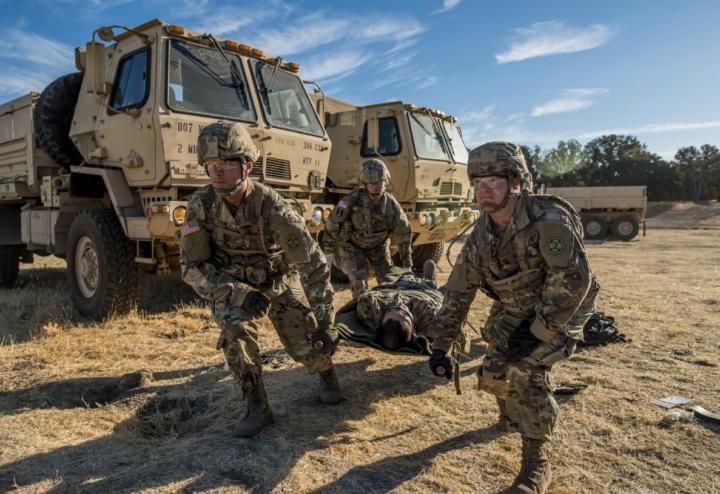 Medical transportation of injured service member on stretcher. Two vehicles are in the background.