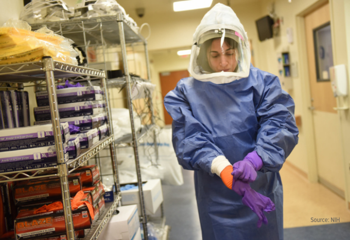 Female scientist fully gowned in containment gear standing next to metal shelves with equipment