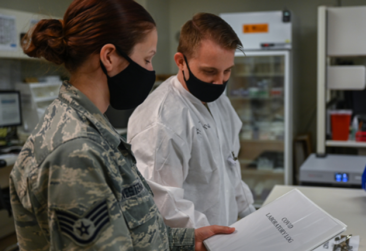 Woman in military uniform stands next to man in lab and shows him paper