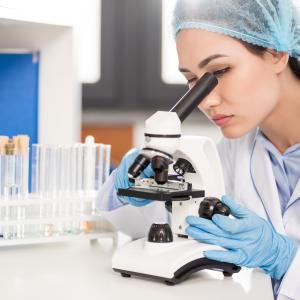 Scientist with microscope and beakers in the background